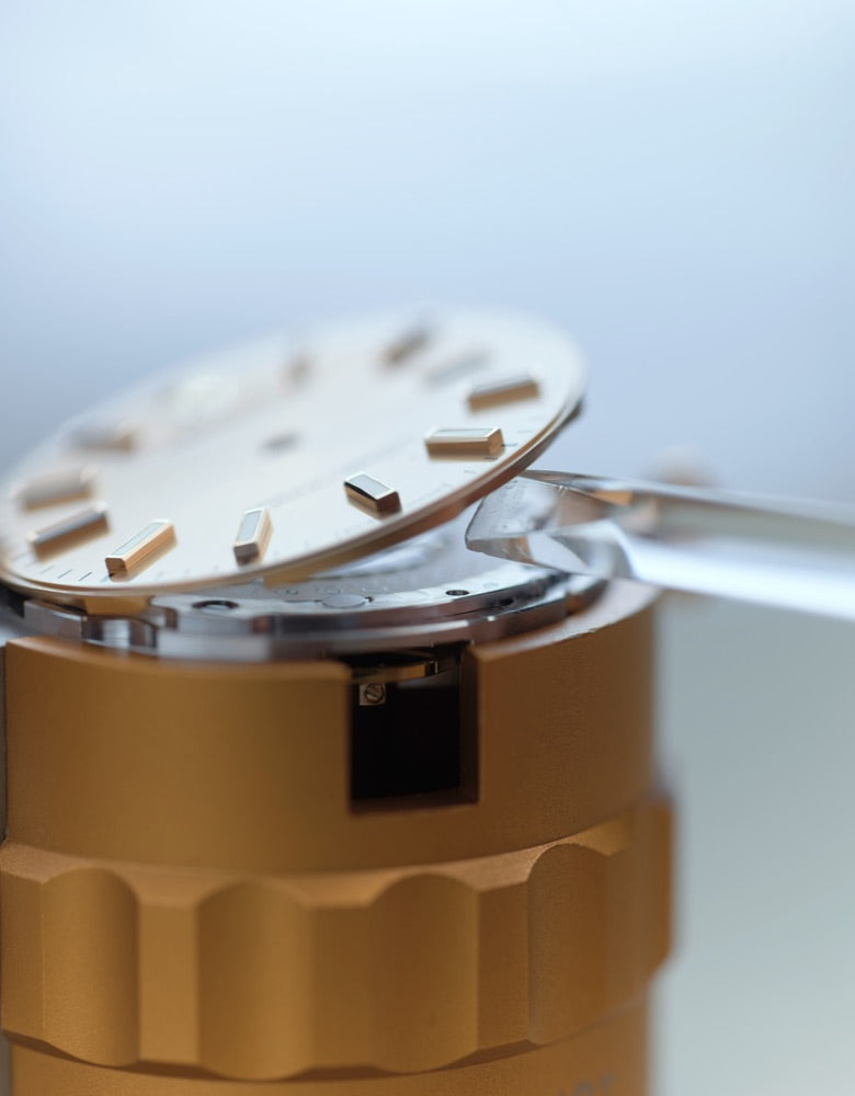 Detailed close‑up showing a watchmaker removing the dial from the movement, highlighting meticulous handling and expert craftsmanship
