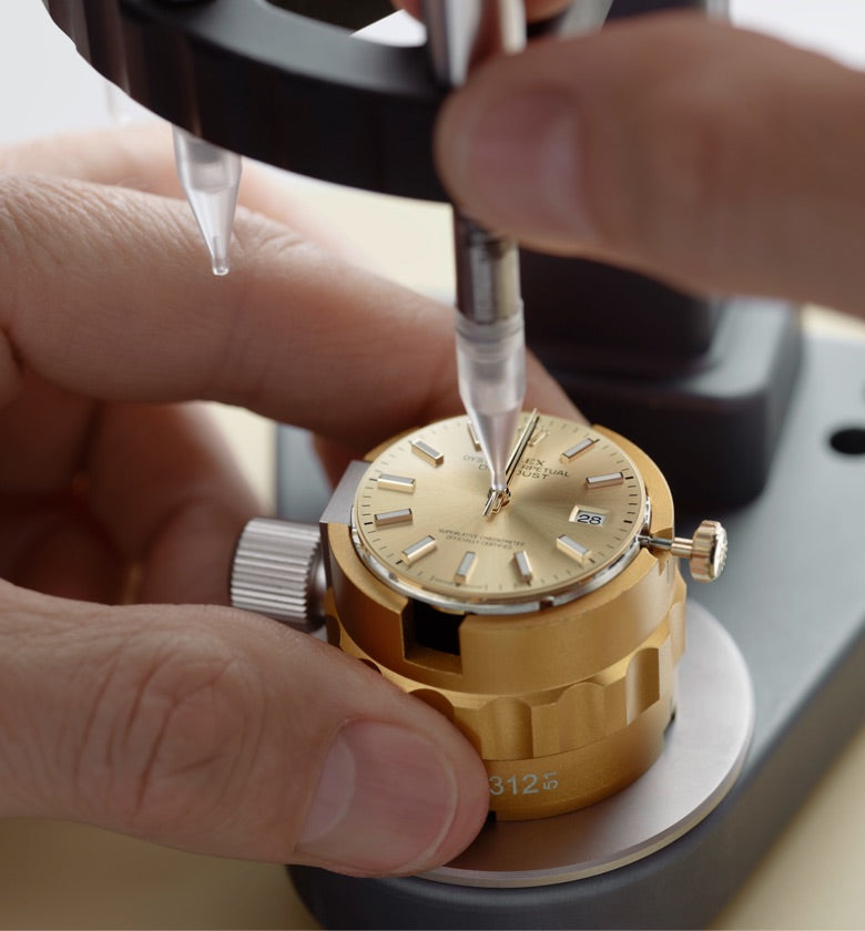 Close‑up image of a watchmaker carefully positioning the watch hands onto the dial using precision tools