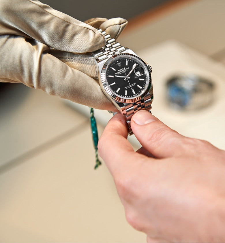 A Rolex expert’s gloved hand presenting a Rolex Datejust to a customer, captured in a close‑up handover moment
