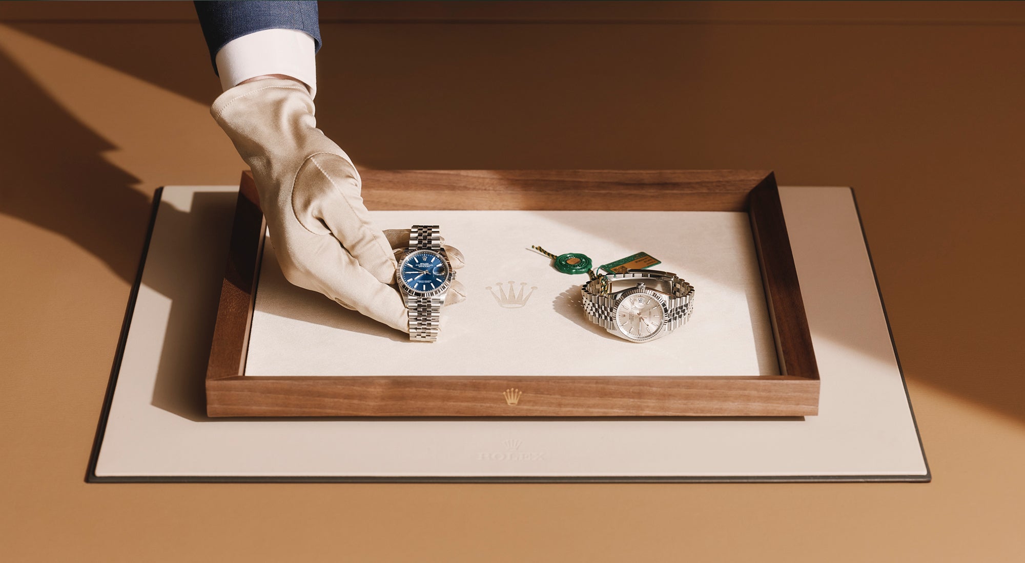 A Rolex expert’s hand gently placing a watch onto a presentation tray that already holds another timepiece, highlighting the care and precision of the retail experience