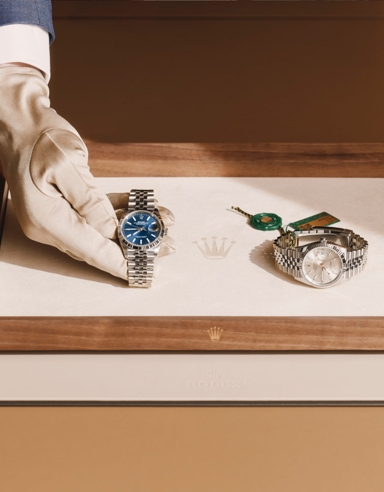 A Rolex expert’s hand gently placing a watch onto a presentation tray that already holds another timepiece, highlighting the care and precision of the retail experience