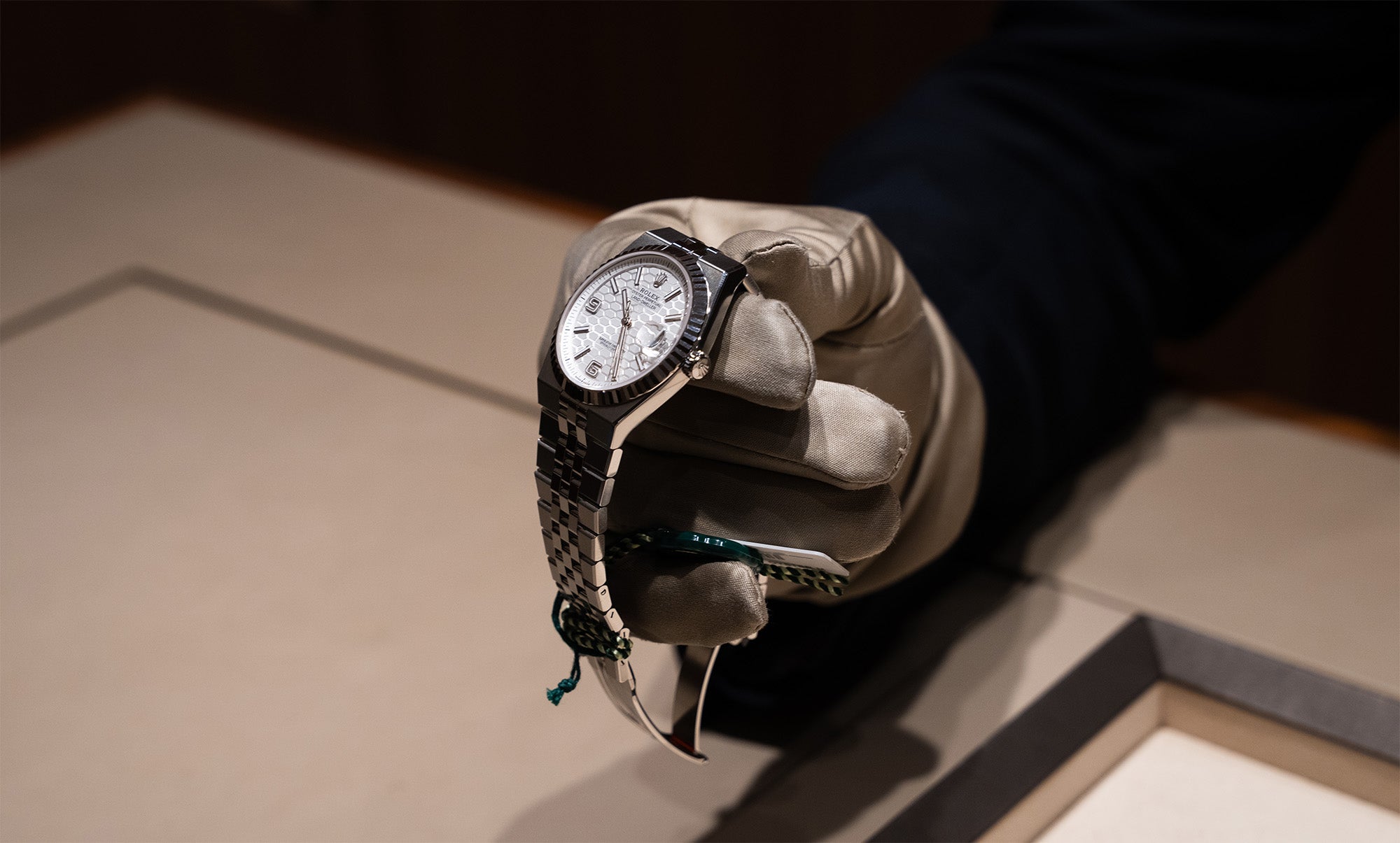 A gloved hand carefully holding a Rolex Land‑Dweller, angled forward in a presenting gesture as though being shown to a customer