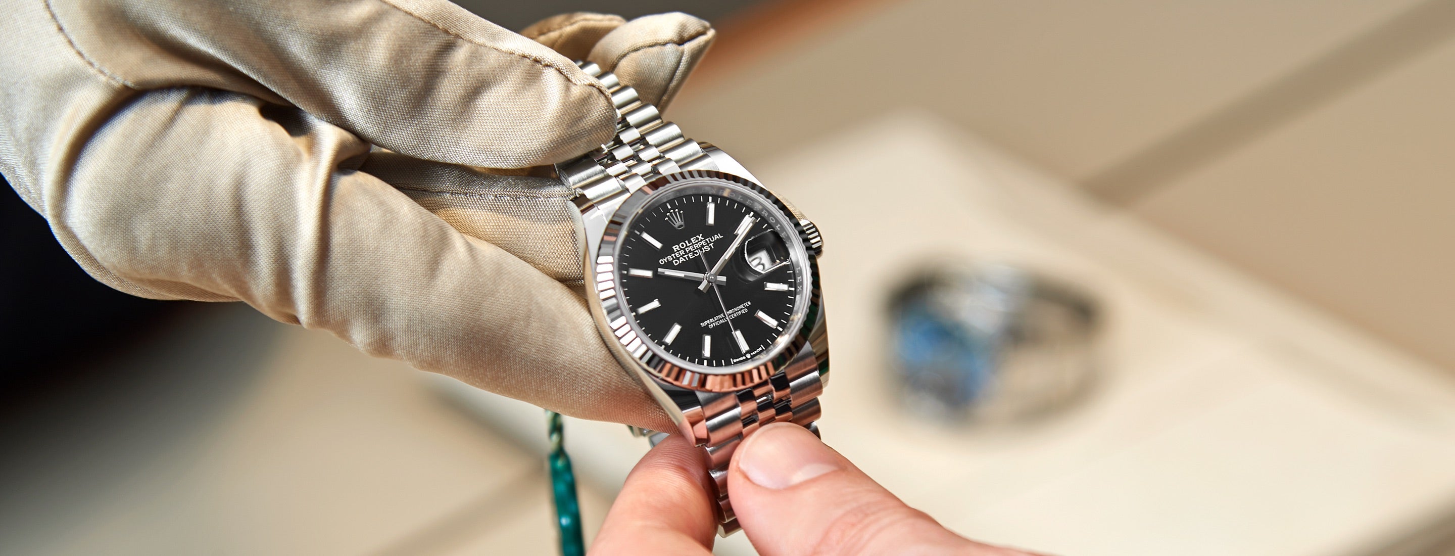 A Rolex expert’s gloved hand presenting a Rolex Datejust to a customer, captured in a close‑up handover moment