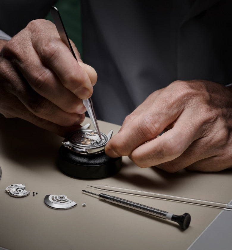 Close‑up image of a watchmaker meticulously dismantling a watch movement, preparing each component for careful inspection
