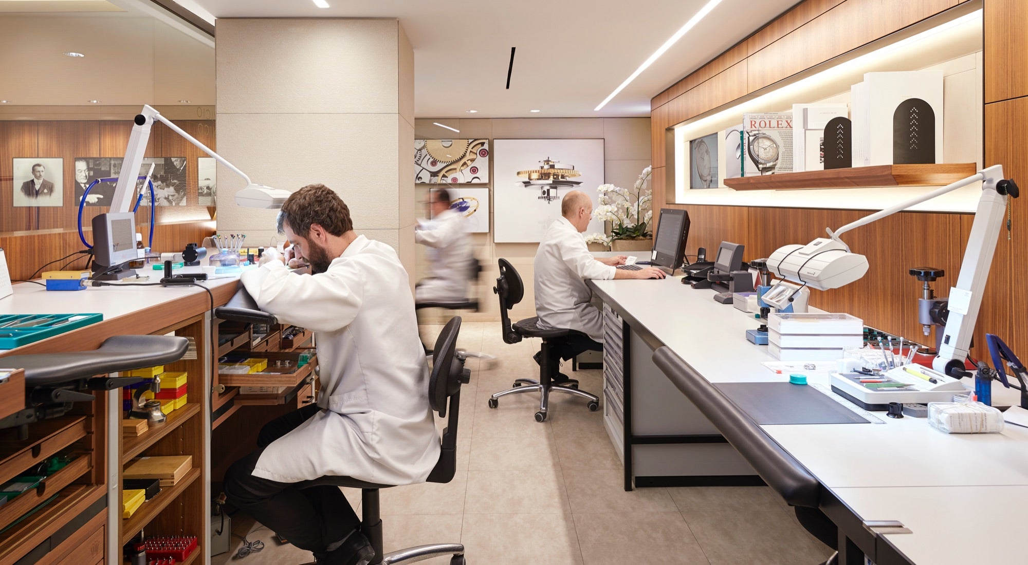 Watchmakers working inside a Rolex workshop, focused at their benches with tools and components around them